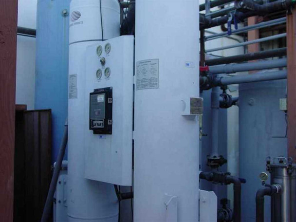 Two large white heatless desiccant air dryer towers with mounted digital controller panel and pressure gauges, blue cylindrical tank at left, overhead piping — side view