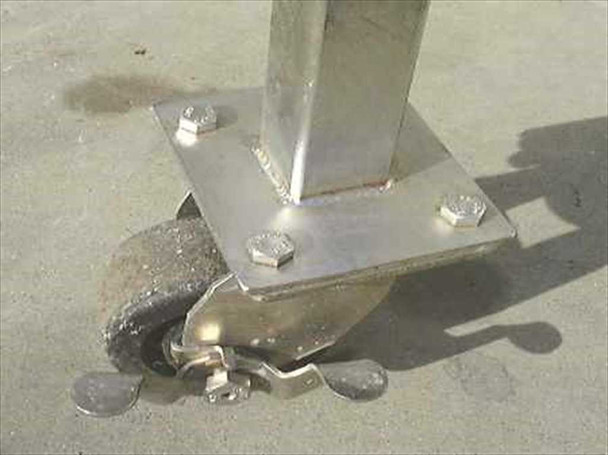 Close-up of bolted swivel caster wheel with locking brake lever attached to stainless steel frame leg base plate