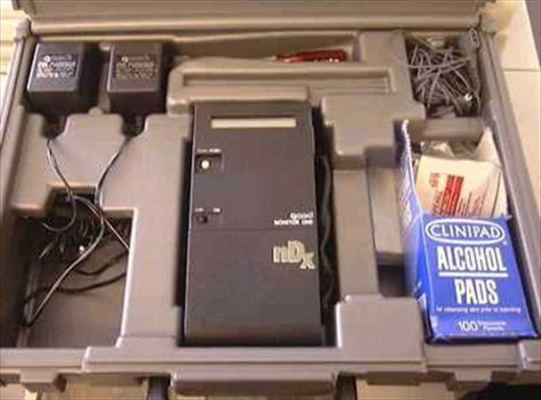 QMED Monitor One nDx heart rate variability monitor shown in open hard plastic carry case with two power adapters, cables, electrodes, and a box of Clinipad alcohol pads