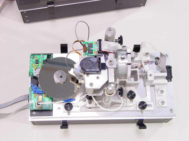 Lotus Technologies 7100 CSS module – interior view with enclosure removed showing hard disk drive under test, spindle motor assembly, optical encoder, PCB with components, and gaging mechanism