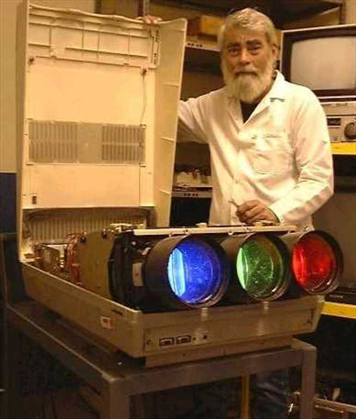 Barco Data 800 CRT projector open with lid raised, three large CRT tubes glowing blue, green, and red, technician in white lab coat standing behind powered-on unit