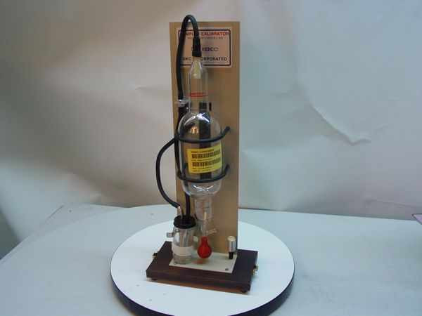 SKC 302 Personal Sampler Calibrator full unit view — glass bubble tube, flexible tubing, and soap reservoir mounted on wooden base