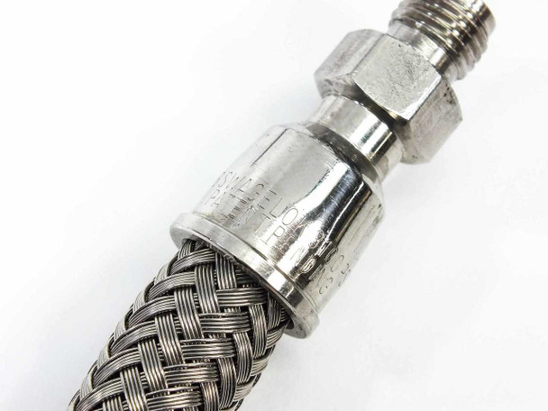 Macro close-up of Swagelok SS-FM4PM2PM2-12 end fitting crimp collar and stainless wire braid detail showing stamped markings on the ferrule