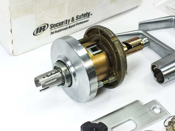 Schlage AL53PD lock chassis assembly close-up showing machined brass and steel cylindrical body with spindle, beside Saturn lever handles and strike plate