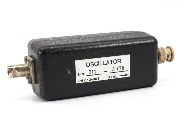 Inficon IPN 013-001 Crystal Oscillator – top view showing white label with part number, serial number 011-3078, and XTAL arrow marking, with BNC connectors on each end