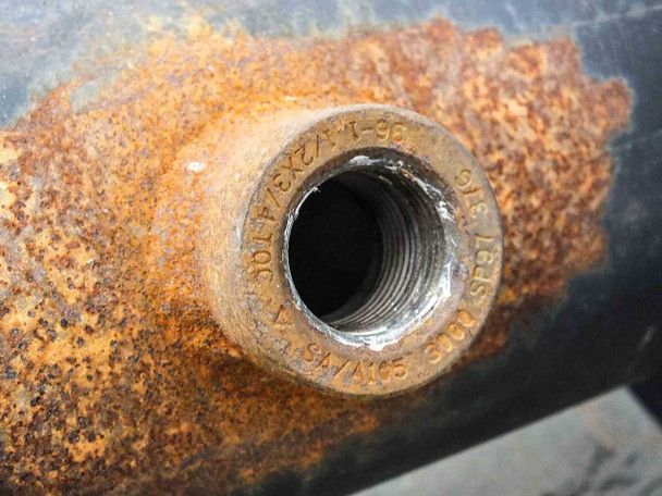Second mid-body threaded port showing stamped markings SA/A105 and threading detail with surrounding heavy rust on pipe surface
