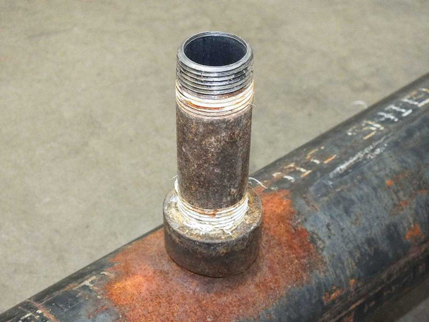 Close-up of mid-body threaded pipe nipple showing male NPT threads — chrome-plated or clean threaded end protruding from rusted boss on pipe body
