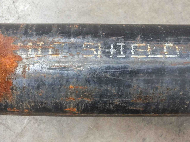 Pipe body showing MIC SHIELD lettering stenciled in white paint on black-coated steel surface with surrounding rust