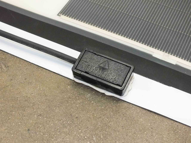 Close-up of black junction box on SoloPower flexible solar panel edge marked DANGER — electrical output connection point
