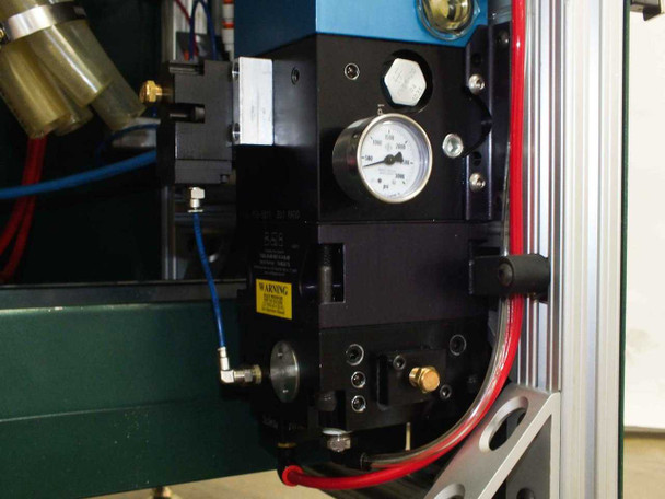 TASQ-30-00-060 30:1 air-driven intensifier pump close-up — black body with pressure gauge, warning label, brass fittings, and blue/red hydraulic lines connected