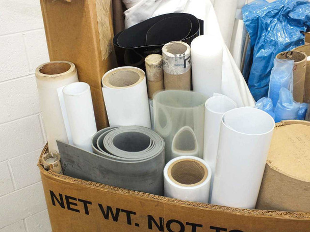 Close-up interior view of pallet box showing gray film roll, white film rolls of various diameters, black sheet material, and translucent clear film rolls