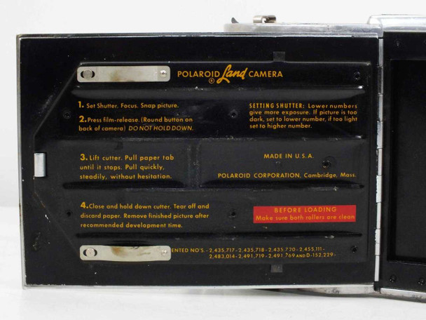 DuMont 297 Polaroid Land Camera interior — closeup of instruction panel showing shutter, film-release, paper-tab, and cutter steps; 'MADE IN U.S.A. POLAROID CORPORATION Cambridge Mass.' text visible