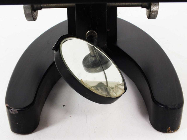 Underside of horseshoe base showing circular substage mirror with dust and debris; paint chipping visible on base feet