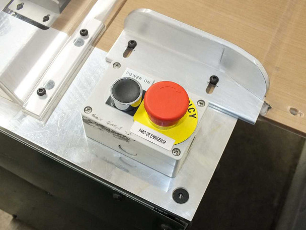 Control panel close-up – Power On pushbutton and red emergency stop button labeled PARO DE EMERGENCIA on aluminum panel