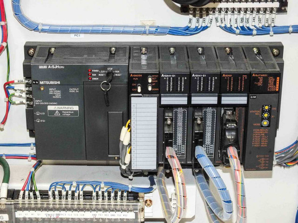 Mitsubishi MELSEC A-Series PLC rack installed in USHIO B0048 cabinet – A1SJHCPU, A1S62DA, two A1SX41-51 modules, A1SY81, and A1SJAR21 modules visible