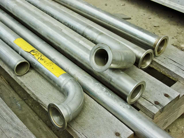 Stainless steel pipes with yellow inventory tag – mix of straight lengths and elbow sections, flanged ends