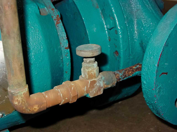 Close-up of pump seal area and copper tubing with fitting and valve showing mineral deposits and corrosion