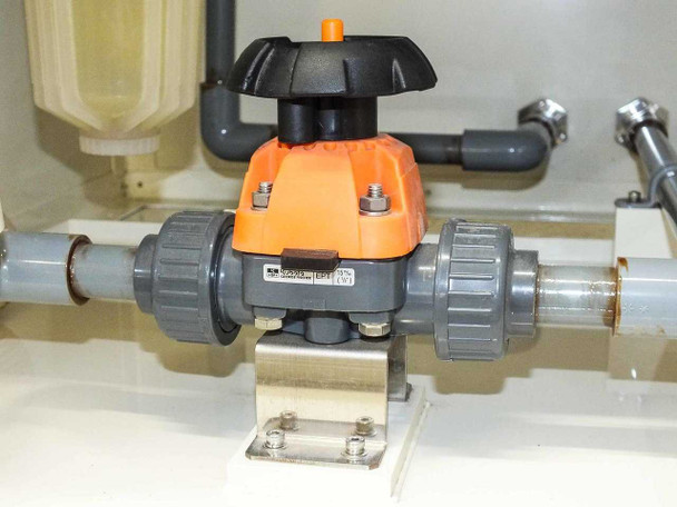 Close-up of orange and black PVC true union ball valve mounted on gray PVC pipe inside enclosure