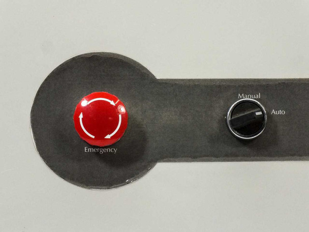 Close-up detail of emergency stop button labeled 'Emergency' with twist-to-release arrows and Manual/Auto rotary selector switch on the enclosure door plate