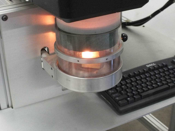 Synrad Fenix Flyer CO2 laser scan head close-up with galvo assembly illuminated and firing, Dell keyboard visible below