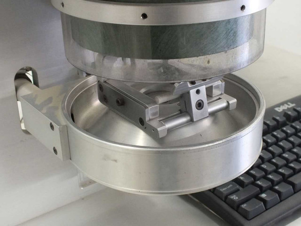 Synrad Fenix Flyer laser scan head underside view showing 2-axis galvo mirror assembly inside circular aluminum housing with workholding fixture mounted