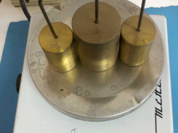 Mettler E2000 calibrated brass test weights on scale pan – three 200g weights visible with markings