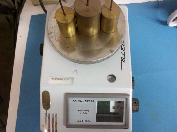Mettler E2000 being tested with three brass calibrated weights on the platform, display and scale lit