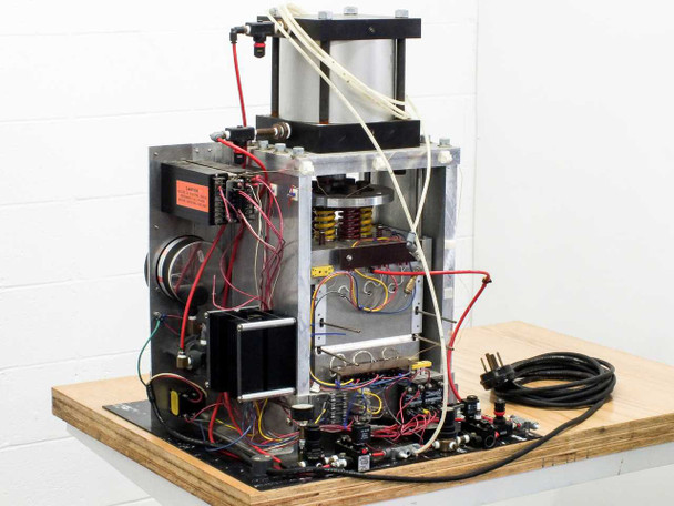 Rear view of press assembly showing pneumatic cylinder, spring platen, control wiring, and solenoid valves on base