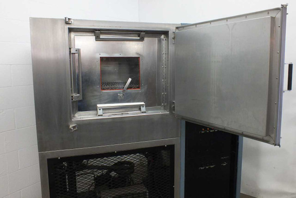Blue M FR-256PB-1 chamber door open — stainless steel interior visible with inner access port/window, wire shelf rack, and door gasket seal