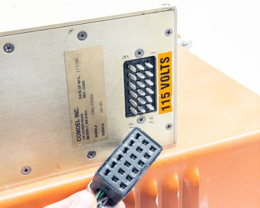 Comdel CPS-200AX RF power supply bottom label and 115 VOLTS warning sticker with multi-pin connector plug visible