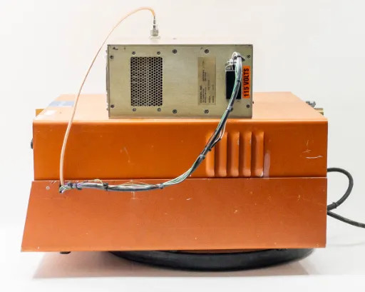 Tegal PlasmaLine 200 rear-left view showing side ventilation fins, Comdel CPS-200AX on top, interconnecting coaxial and signal cables, and base turntable