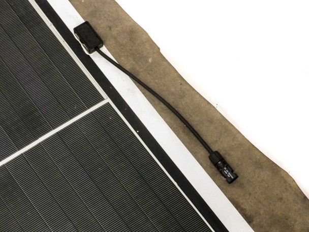 Close-up of MC4 cable junction box area at panel edge, showing short pigtail cable and MC4 connector body against the flexible panel substrate
