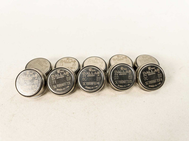 Lot of 10 Dallas Semiconductor DS1982U-F5 iButton stainless steel disk EPROM data carriers arranged in two rows on white surface