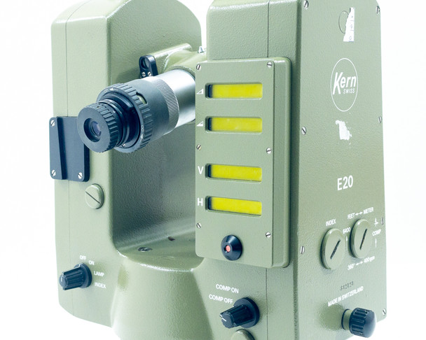 Kern E20 Theodolite three-quarter view showing illuminated vertical (V) and horizontal (H) yellow scale windows, COMP ON/COMP OFF controls, eyepiece, and front panel