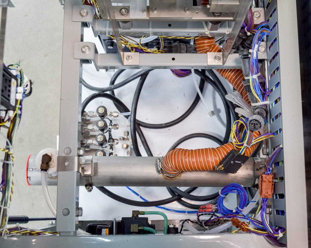 Internal lower chassis view showing orange-wrapped heating coil assembly, stainless manifold block with fittings, black high-voltage wiring, thermocouple wiring, and aluminum structural rails