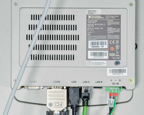 Rear of National Instruments TPC-2230 touchscreen computer showing COM1, COM2, USB, LAN A, LAN B, and DC IN ports with cables connected