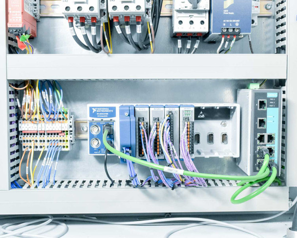 Electrical enclosure lower section showing National Instruments NI cDAQ or similar modular controller chassis with blue I/O modules and green Profinet cabling