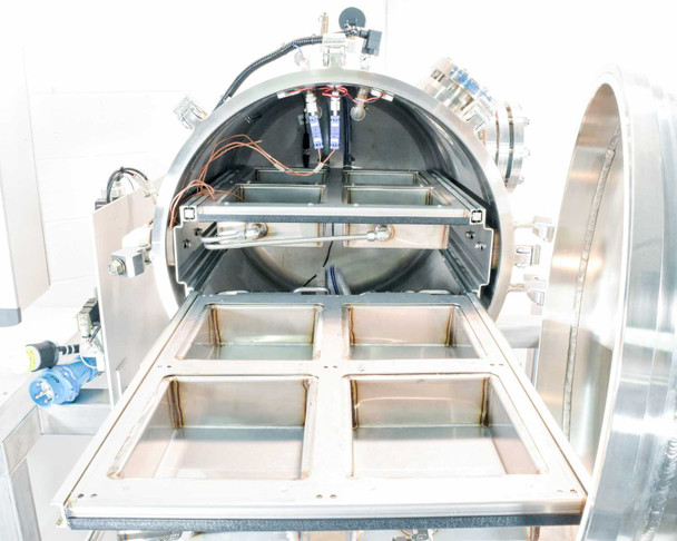 Vacuum chamber open with four stainless steel sample trays partially extended on slide rails, internal wiring and fittings visible