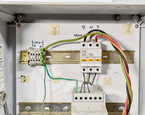 Close-up of control enclosure interior showing 480V three-phase wiring labeled B, W, R and 110V neutral connections on DIN rail
