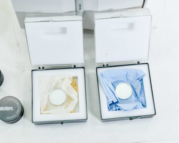 Two Labsphere certified reflectance standard boxes open showing white diffuse reflectance disk standards in protective packaging; Labsphere SRS-99-010 canister visible at left