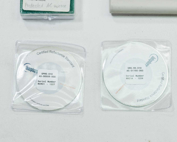 Close-up of two Labsphere Certified Reflectance Standard disks in sealed bags — SPRS-010 AS-00559-000 Serial MIR01-1227 (left) and SRS-99-010 AS-01160-060 Serial BR21A-1224 (right)