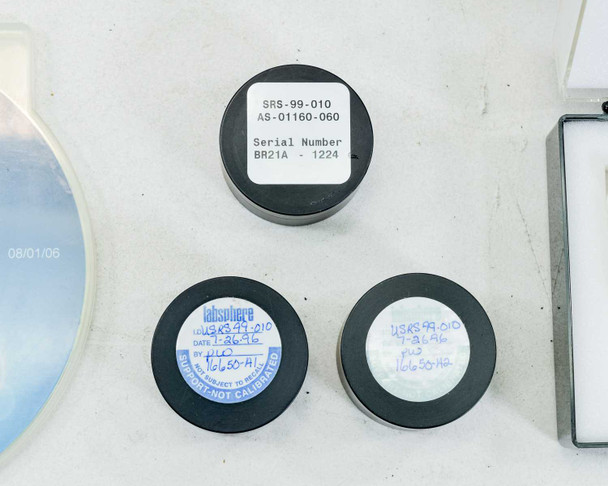 Three Labsphere calibration standard puck holders — SRS-99-010 AS-01160-060 Serial BR21A-1224 (top), two additional Labsphere SRS-99-010 pucks with date and calibration labels (bottom)