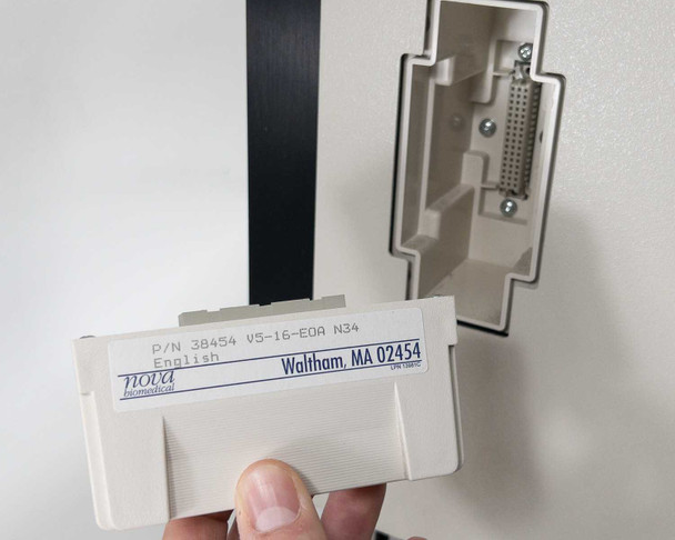 Nova Biomedical BioProfile 100 Plus – cartridge P/N 38454 V5-16-EOA N34 English label held by hand next to cartridge slot on instrument