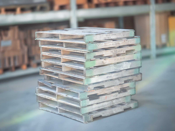 Stack of approximately ten 48x48 wooden pallets in warehouse showing weathered and green-painted edges
