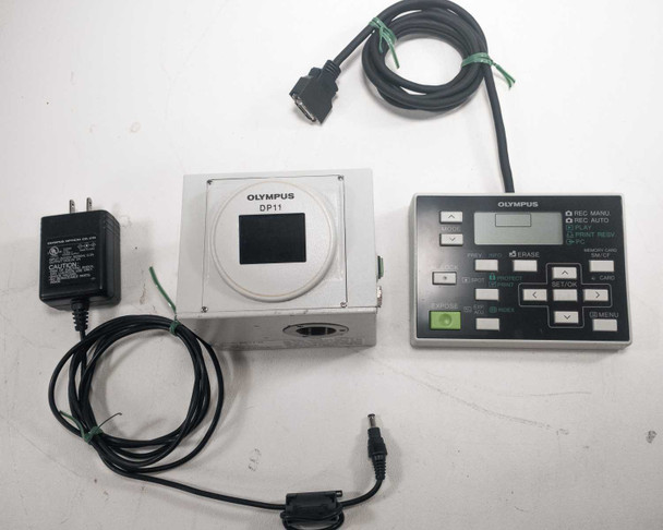Olympus DP11-N full kit laid out — camera body, hand switch controller, AC charger, and RS-232C cable