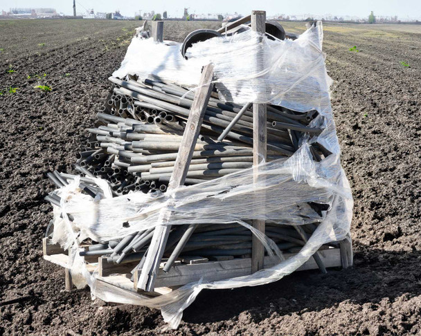 Close angled view of pallet showing bundled poly irrigation pipe sections and coils in assorted diameters including straight lengths and bent pieces