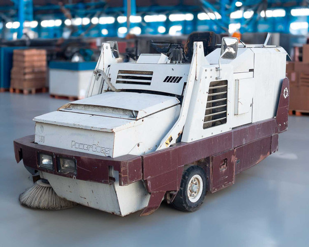 PowerBoss TSS/80-HD propane riding sweeper scrubber — front three-quarter view showing side brush, front bumper, and white and maroon body in warehouse