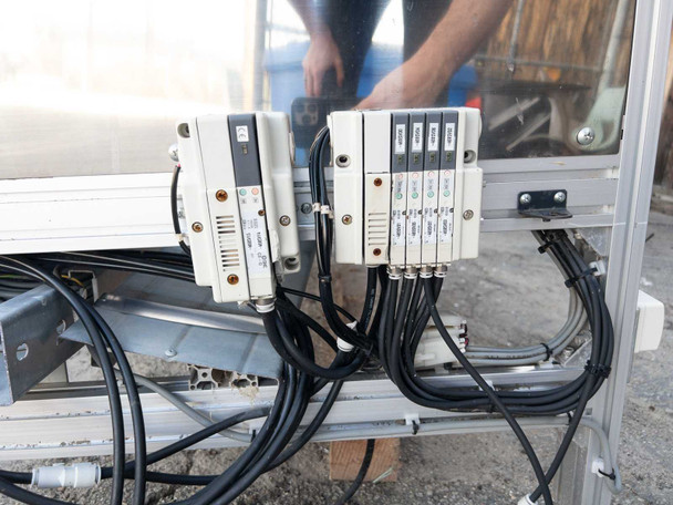SMC pneumatic solenoid valve manifold mounted to conveyor frame – multiple valves and pneumatic tubing visible