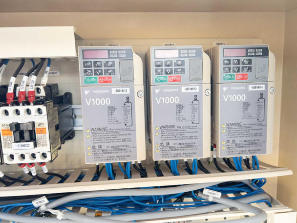 Close-up of three Yaskawa V1000 variable frequency drives inside control cabinet with display panels and wiring