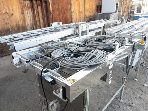 Excel Flow SC23460 conveyor section showing stainless steel frame with coiled gray cables on roller bed – side-angle view